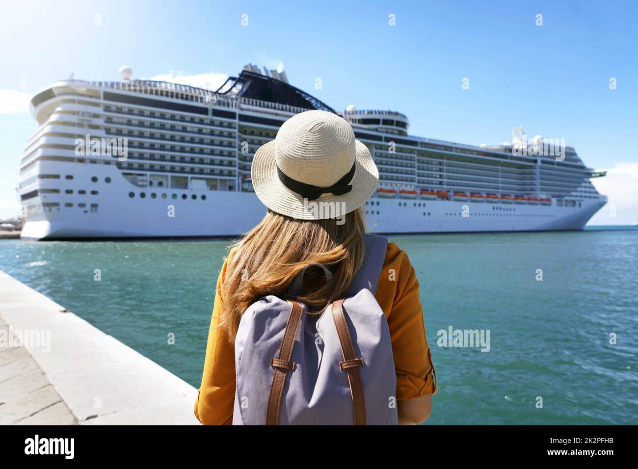 Kreuzfahrturlaub. Rückansicht des Touristenmädchens mit Rucksack und Hut vor dem großen Kreuzschiff. Stockfoto