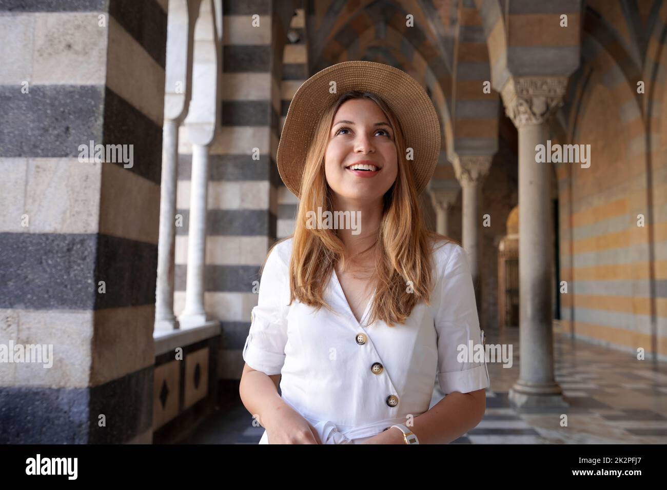 Die schöne junge Frau schaut auf, wenn sie in der Kolonnade vor der Amalfi-Kathedrale in Italien spazieren geht Stockfoto