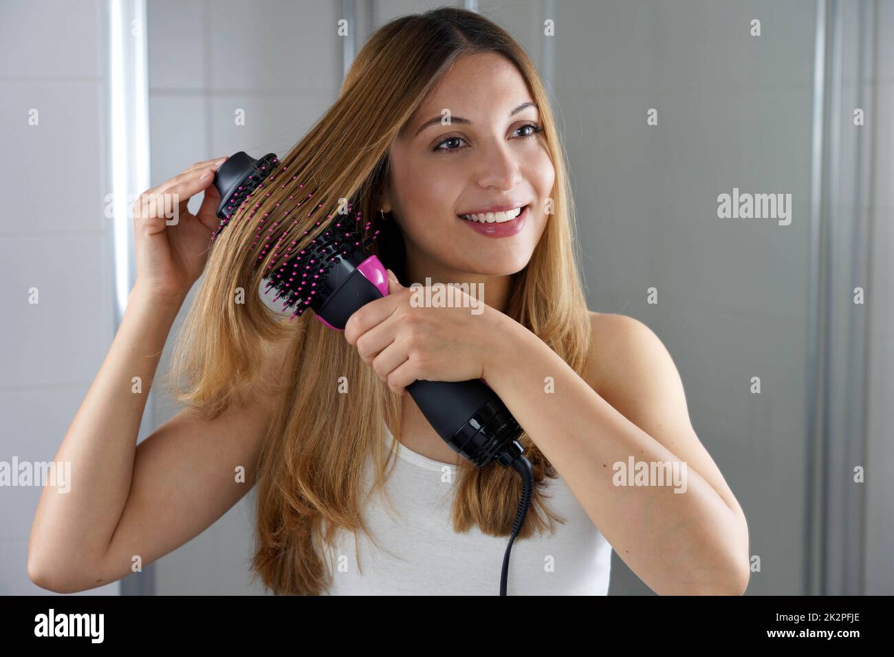 Die junge Frau hält einen runden Bürstenfon, um das Haar zu Hause auf einfache Weise zu stylen Stockfoto