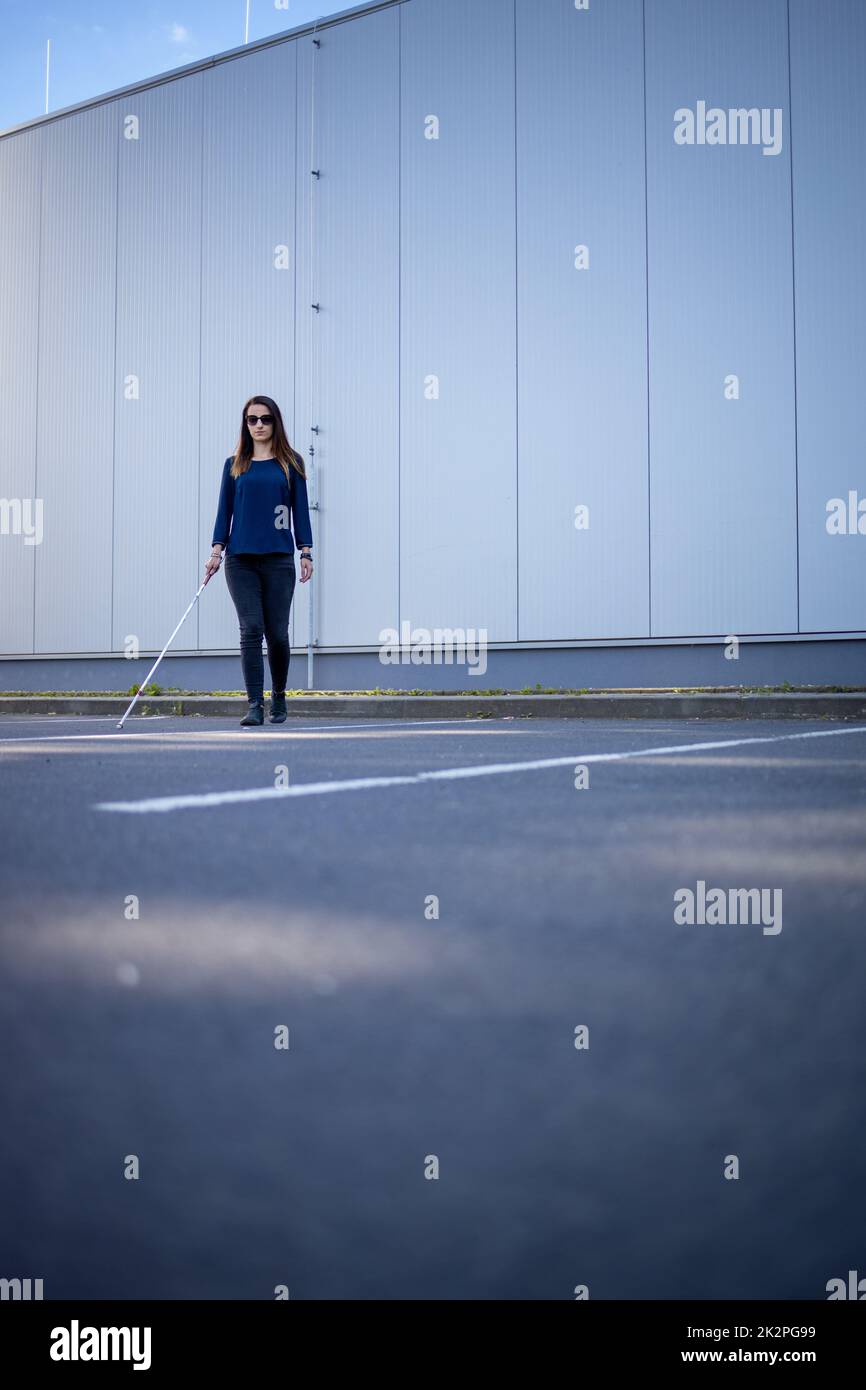 Junge Frau mit Sehbehinderung geht auf den Straßen der Stadt und nutzt ihren weißen Stock, um besser durch den städtischen Raum zu navigieren und sicher an ihr Ziel zu gelangen Stockfoto