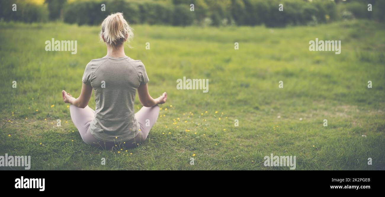 Frau, die in aktiver Kleidung in Lotusposition in der Natur sitzt. Stockfoto