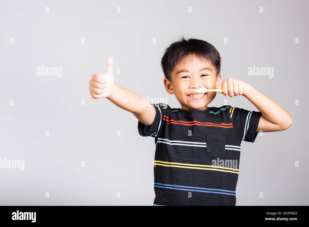 Kleiner süßer Junge, 5-6 Jahre alt, lächelt Zähne putzen und zeigt Daumen hoch, um ein gutes Zeichen zu geben Stockfoto