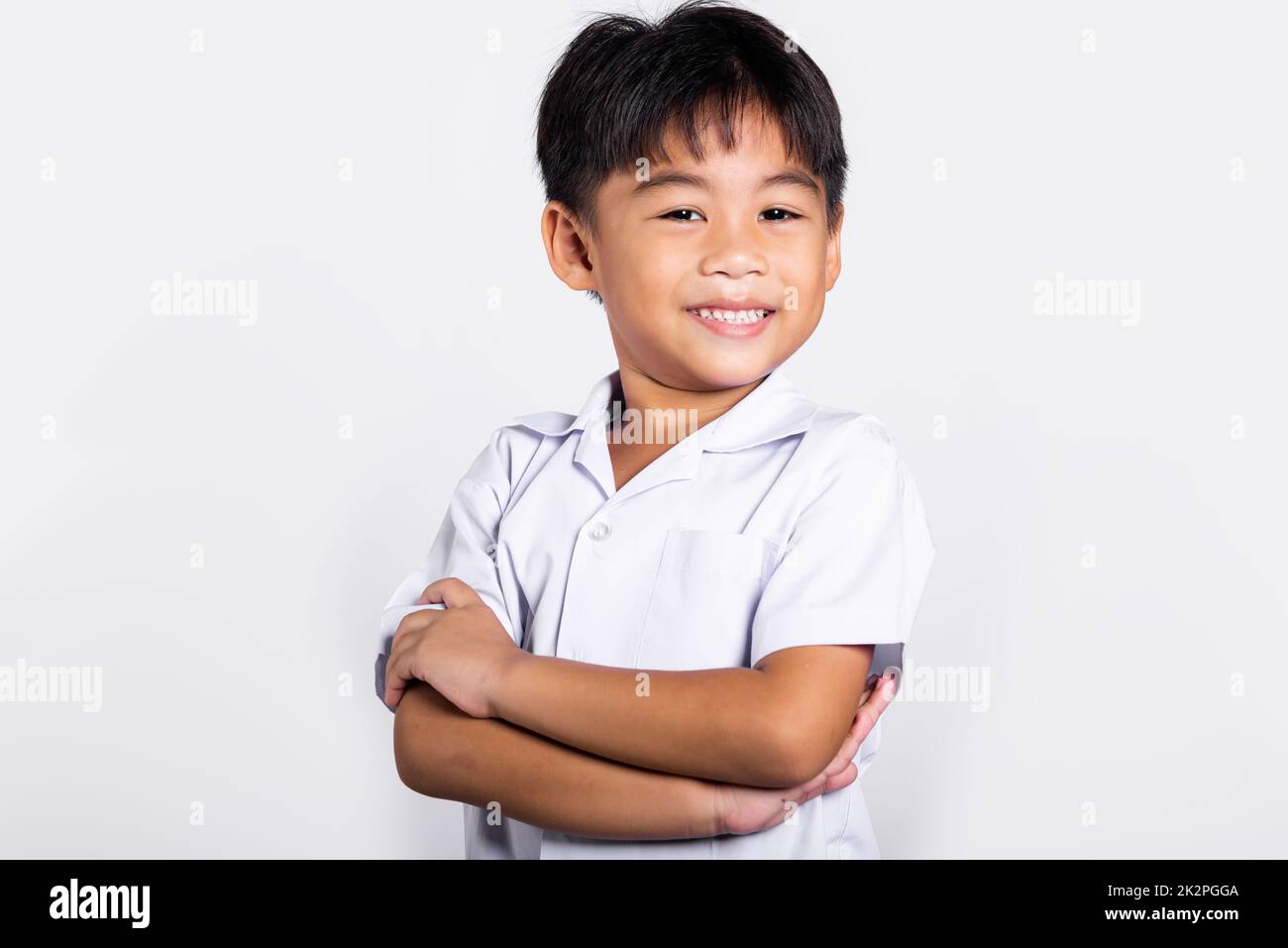 Asiatisches Kleinkind lächelt fröhlich und trägt Thai-Uniform, rote Hosen stehen mit zusammengeklappten Armen Stockfoto