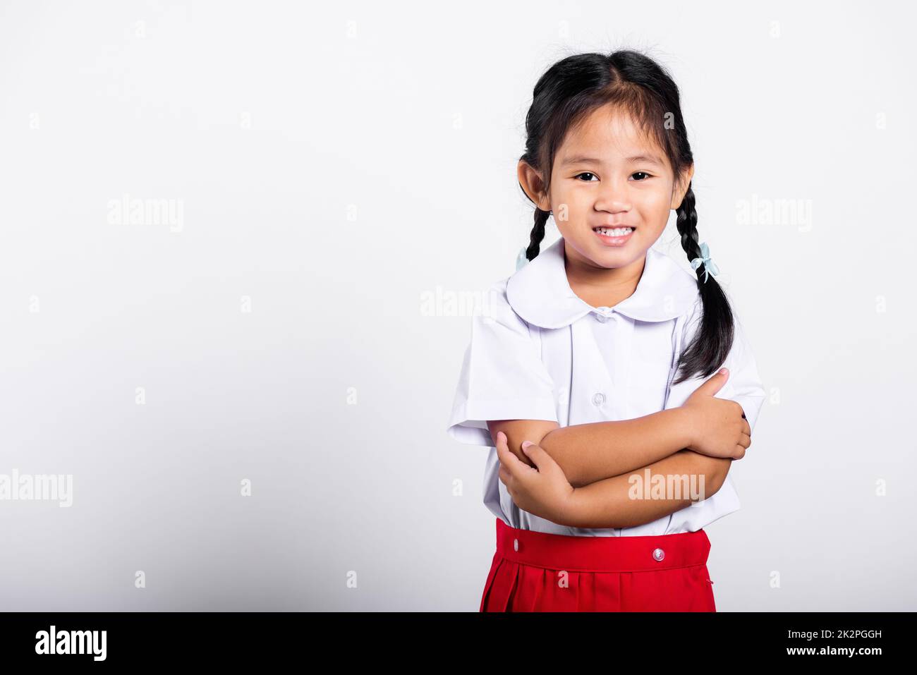 Asiatisches Kleinkind lächelt fröhlich und trägt Thai-Uniform als Studentin, roter Rock mit zusammengeklappten Armen Stockfoto
