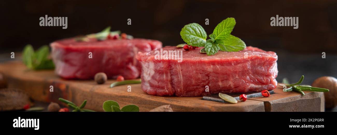 Rohe Rinderfilet-Steaks mit Kräutern und Gewürzen auf einem dunklen Tisch aus nächster Nähe Stockfoto