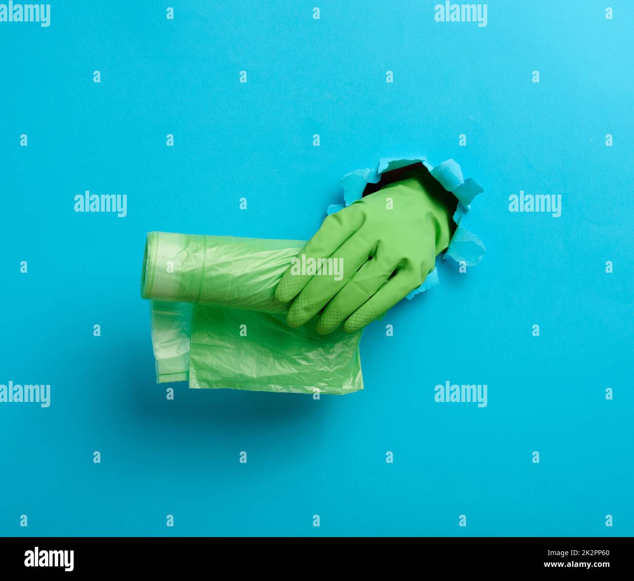 Die Hand hält ein Paket transparenter Müllbeutel auf blauem Hintergrund. Ein Teil des Körpers ragt aus einem zerrissenen Loch im Papier heraus Stockfoto