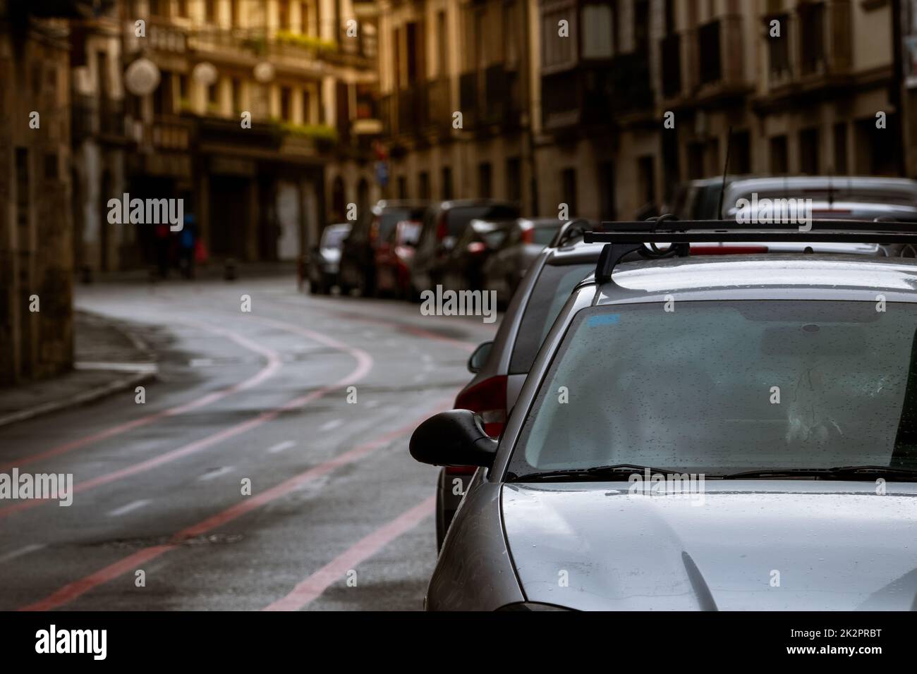 Eine Reihe von Autos, die an der Straße geparkt sind, und alte Gebäude in Europa-Stadt. Viele Autos parken auf der Straße in der Altstadt. Stadtstraße in Europa. Vorderansicht eines Autos, das vor einem Wohngebäude geparkt ist. Stadtverkehr. Stockfoto