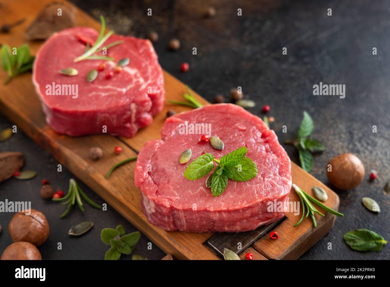 Rohe Rinderfilet-Steaks mit Kräutern und Gewürzen auf einem dunklen Tisch aus nächster Nähe Stockfoto