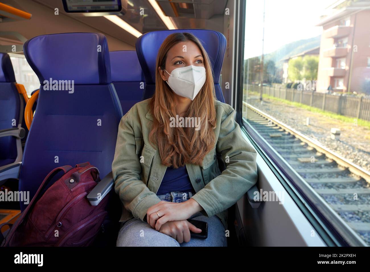 Junge Backpacker-Frau, die mit dem Zug mit Schutzmaske reist Stockfoto