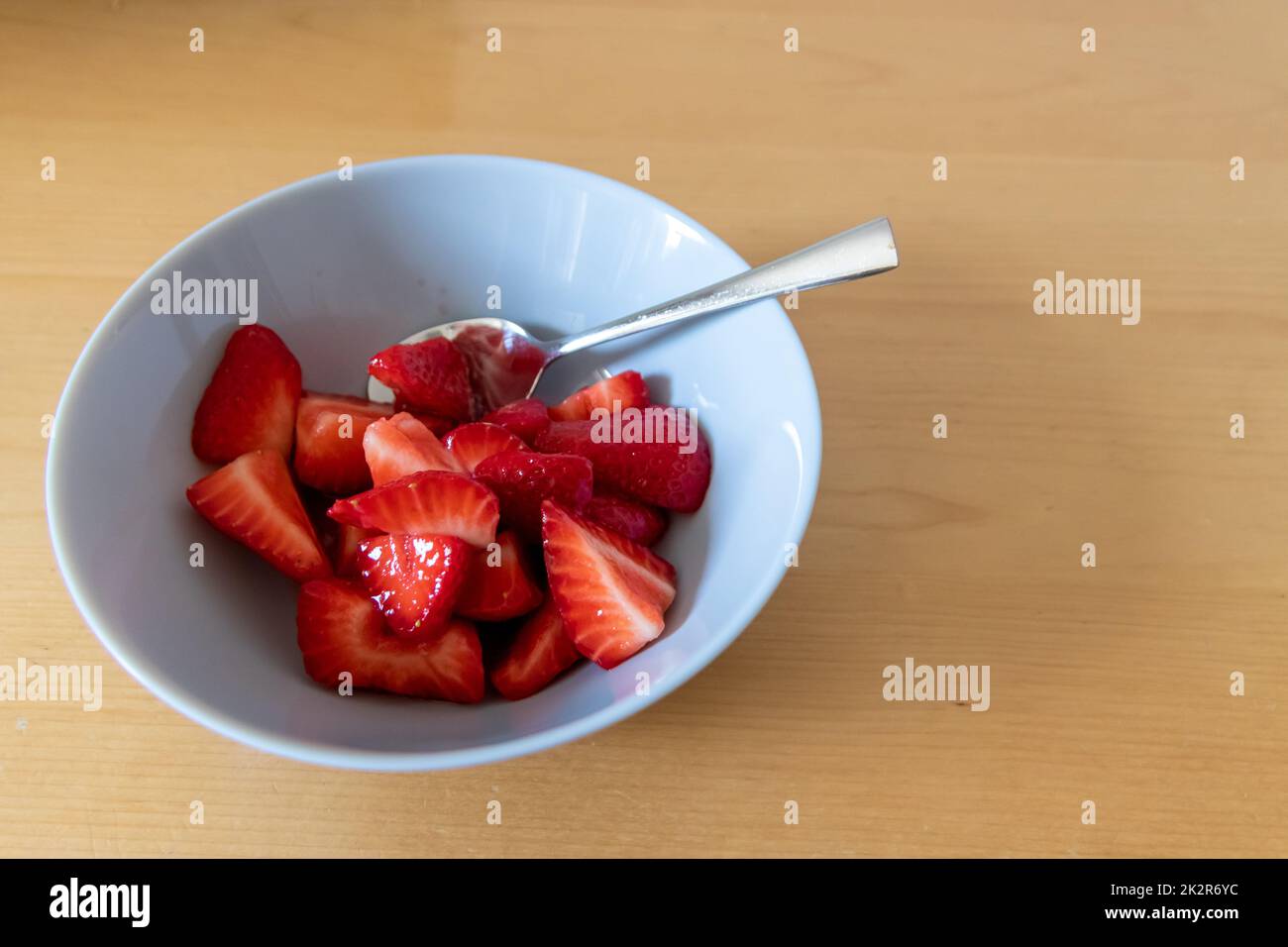 Viele geschnittene Erdbeeren in der Schüssel sind bereit zum Essen mit Silberlöffel oder als leckeres Fingerfood und gesunde Snacks mit roten Früchten und Vitaminen auf einem hölzernen Küchentisch für nachhaltige Ernährung und Gesundheit Stockfoto