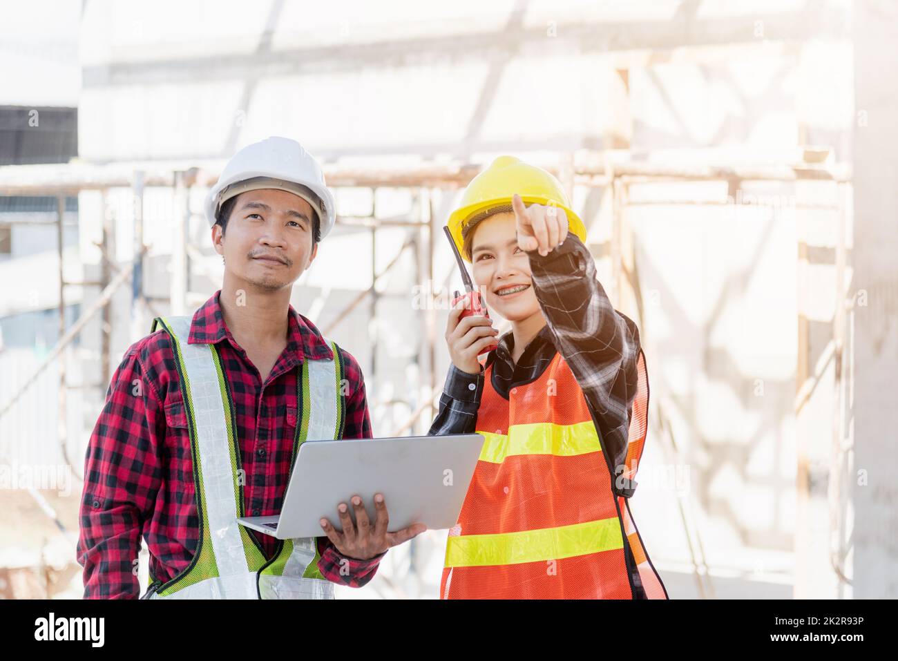 Asiatische Ingenieur Vorarbeiter Mann und Frau, die auf der Baustelle arbeiten, benutzen Laptop und sprechen mit Radio Stockfoto