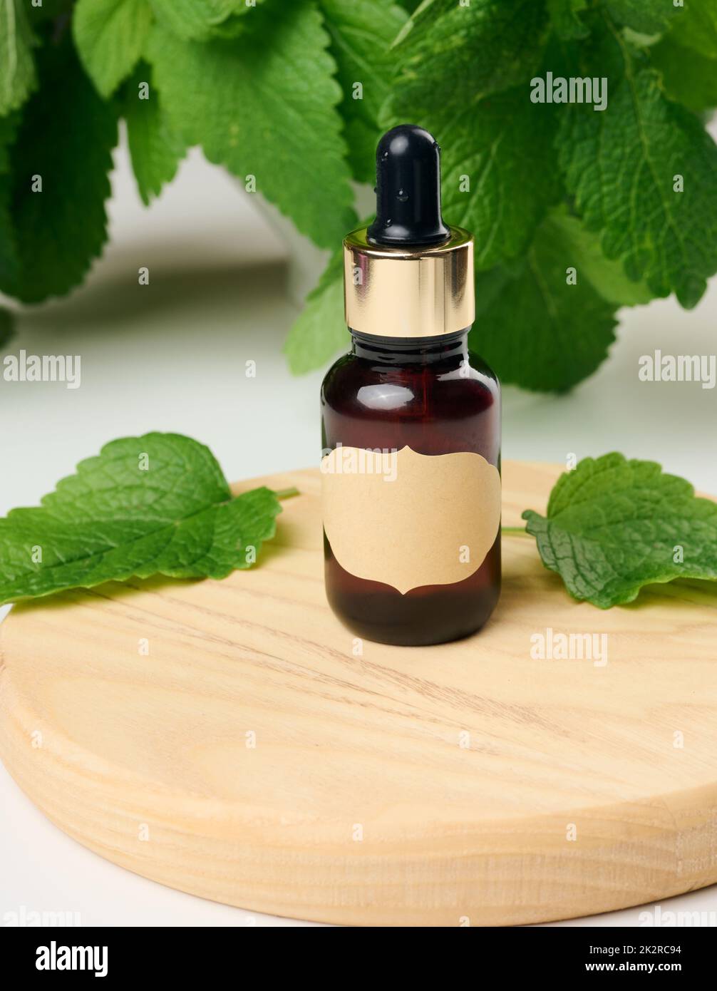 Braune Glasflasche mit Papieretikett und Pipette auf einem weißen Tisch, grüne Minzblätter Stockfoto