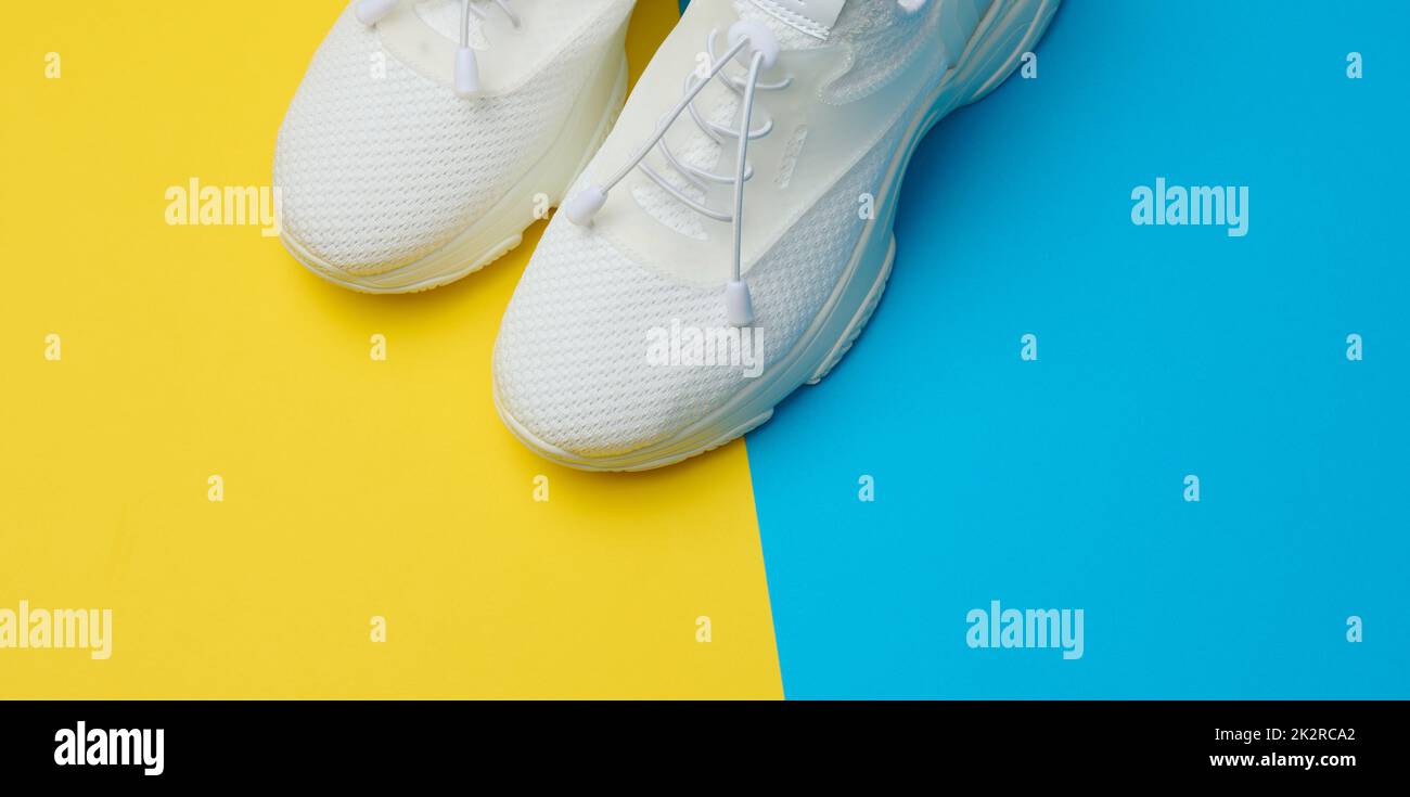 Weiße Textil-Sneakers auf blaugelbem Hintergrund, Draufsicht Stockfoto