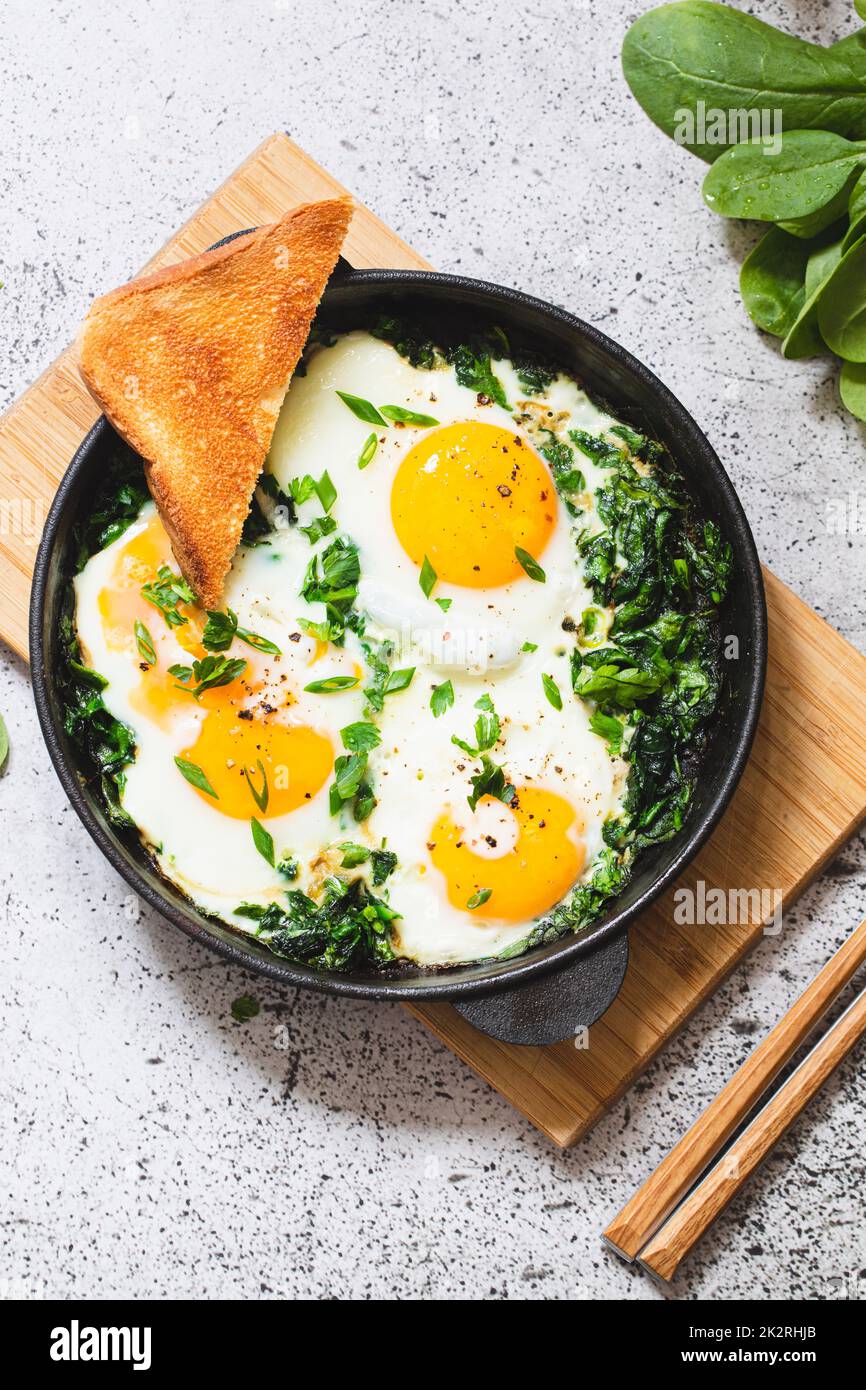 Grüner Shakshuka in einer gusseisernen Pfanne. Spiegeleier mit Spinat und gebratenem Toast. Gesundes, nahrhaftes Frühstück Stockfoto