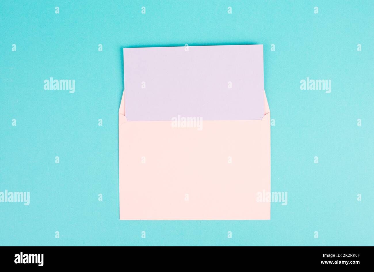 Rosafarbener Umschlag mit leerem Papier auf türkisfarbenem Hintergrund, Kopierraum für Text, Grußkarte, Kommunikations- und Ankündigungskonzept, Erinnerung Stockfoto