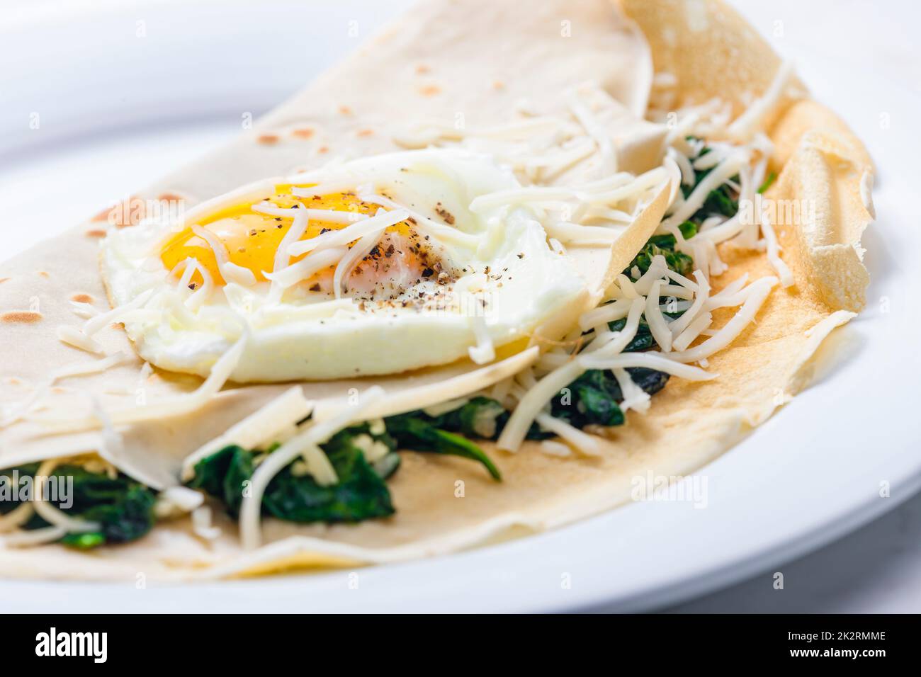 Pfannkuchen gefüllt mit Spinatblättern, serviert mit Spiegelei und geriebenem Käse Stockfoto