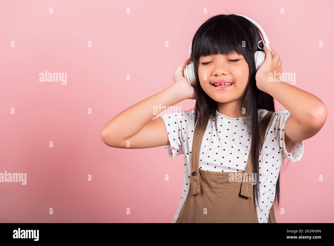 Asiatisches kleines Kind, 10 Jahre alt, lächelnd, hört Musik und trägt ein schnurloses Headset Stockfoto