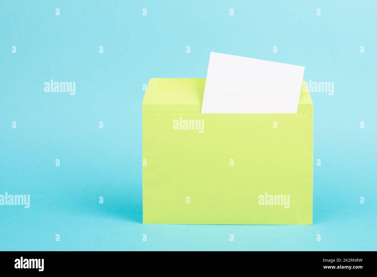 Grüner Umschlag mit leerem Papier auf türkisfarbenem Hintergrund, Kopierraum für Text, Grußkarte, Kommunikations- und Ankündigungskonzept, Erinnerung Stockfoto