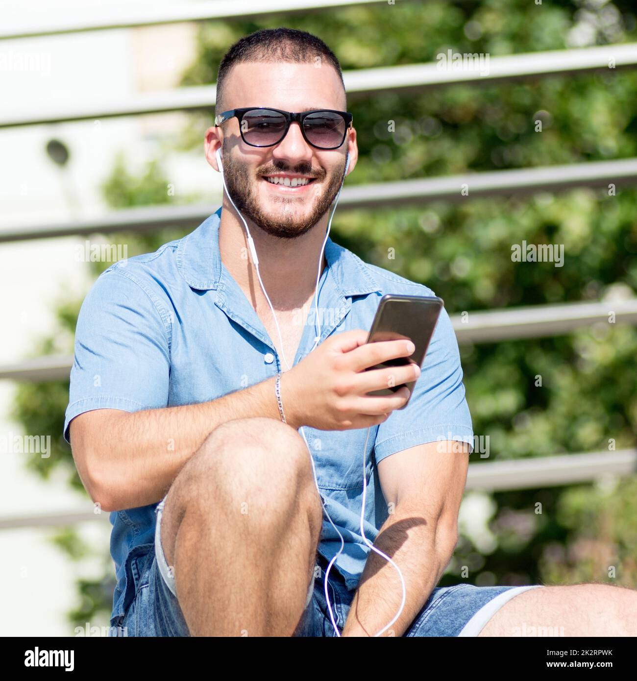 Lächelnder Typ mit Ohrhörern, der telefoniert Stockfoto