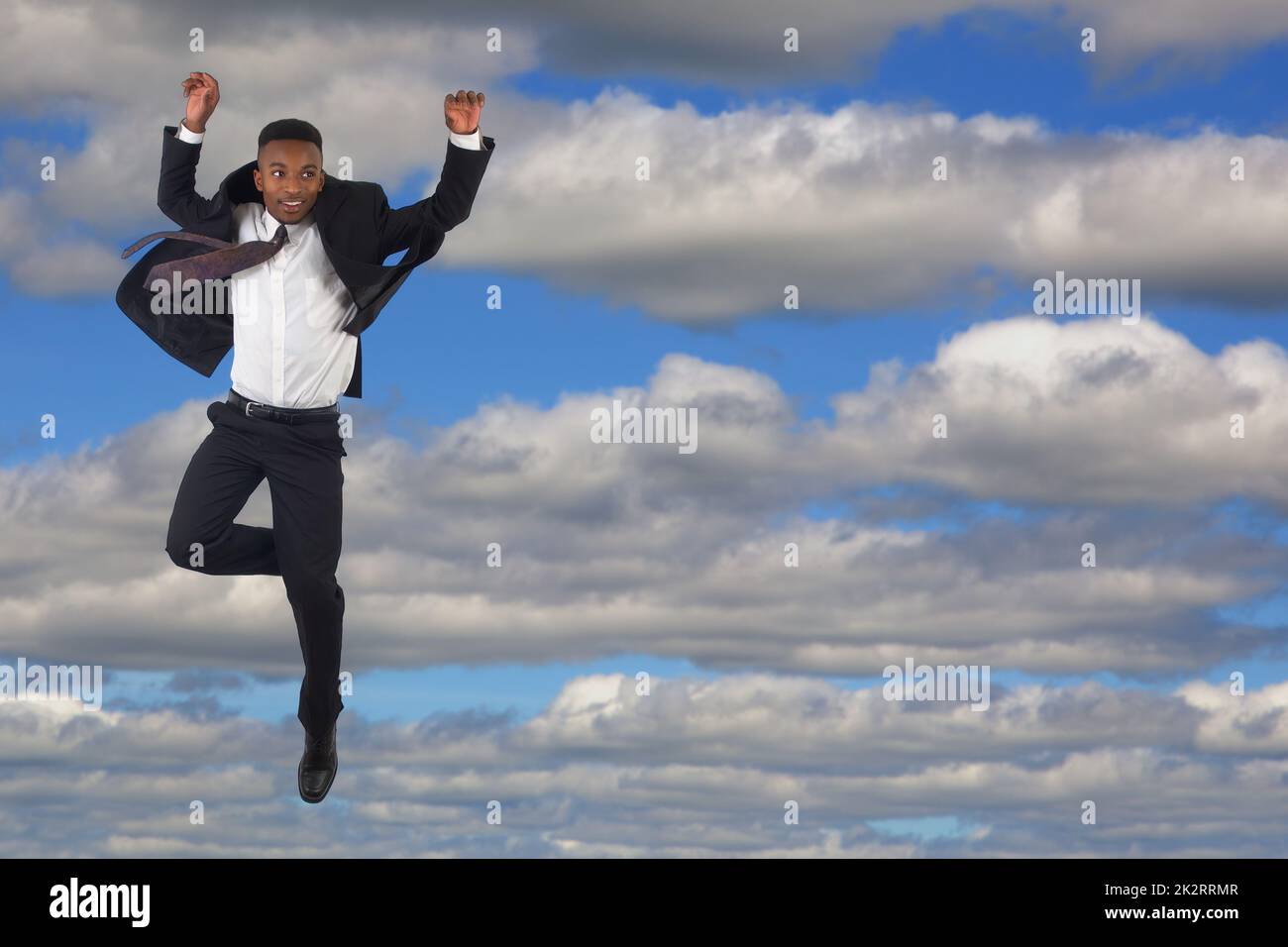 Junger Geschäftsmann mit Anzug und Krawatte, der in den wolkigen Himmel springt, Erfolg hat und Freiheit lebt Stockfoto