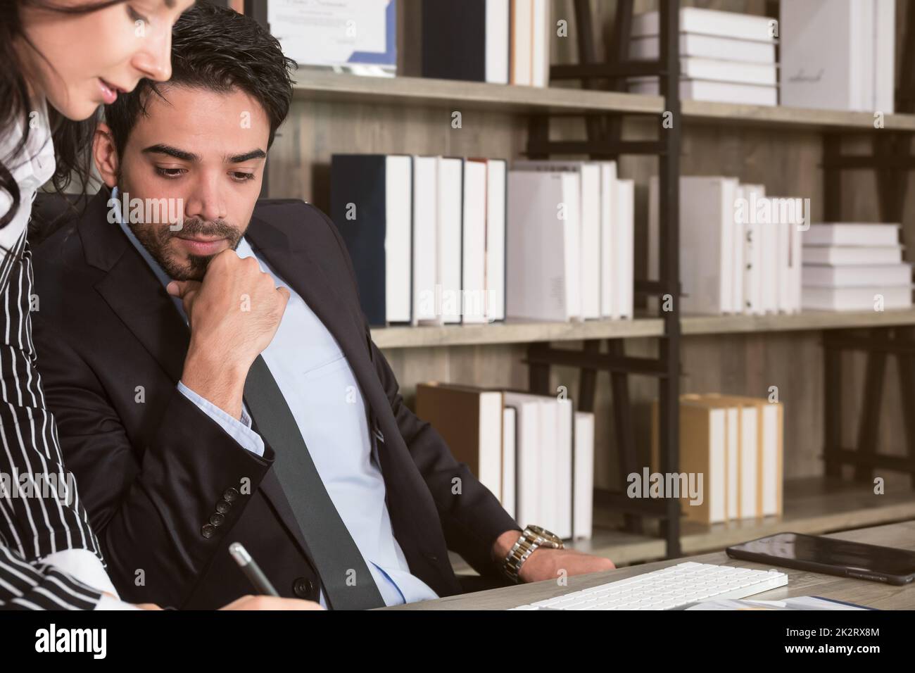 Geschäftsleute arbeiten zusammen und diskutieren über ein neues Projekt. Ein Geschäftsmann saß am Schreibtisch, während eine Geschäftsfrau neben ihm schrieb und stand. Stockfoto