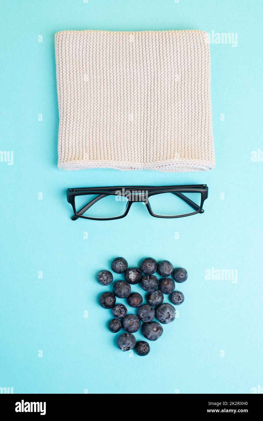 Menschliches Gesicht mit Wollhut, Brille und Blaubeeren als Bart, witziges minimalistisches Porträt, Öko-Freak-Lifestyle, veganes Essen Stockfoto