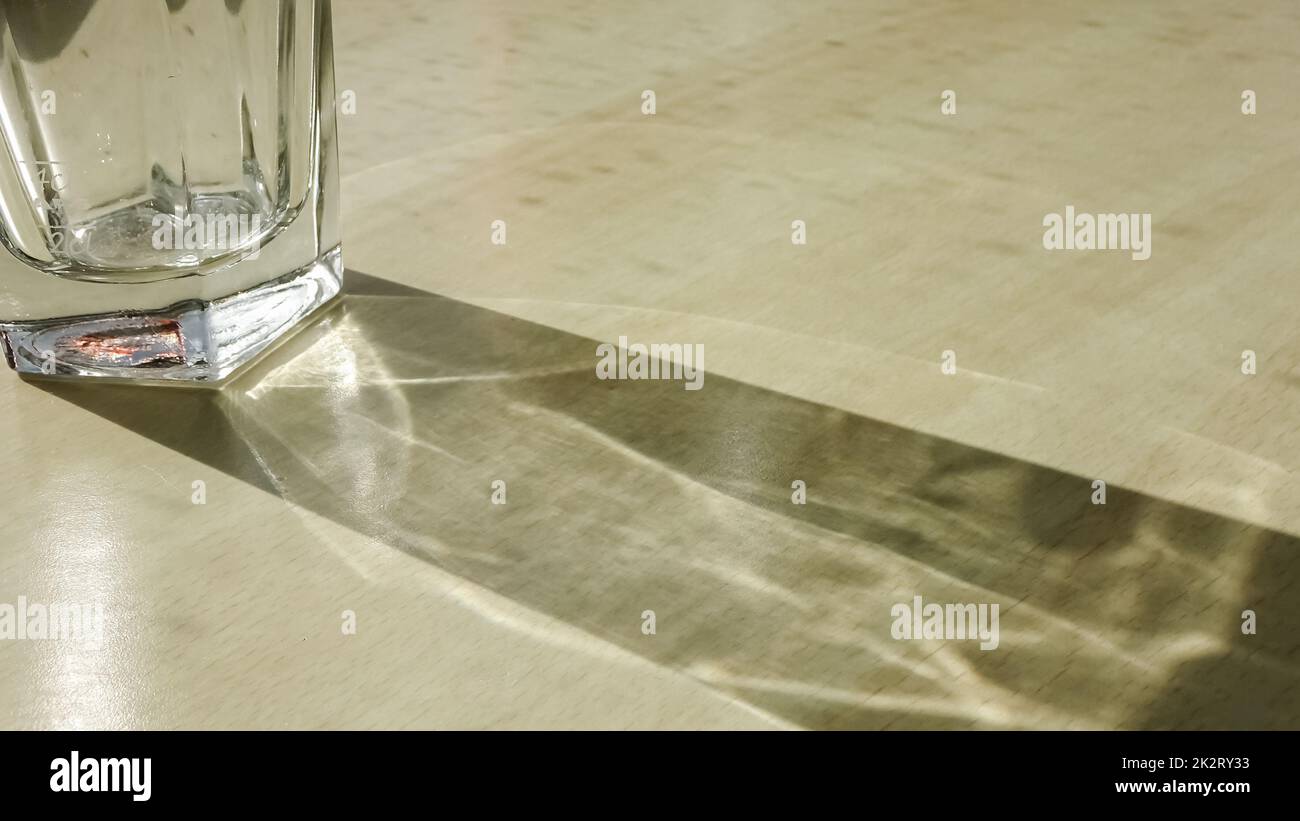 Trinkglas mit ätzenden Lichteffekten auf einem Holztisch. Stockfoto