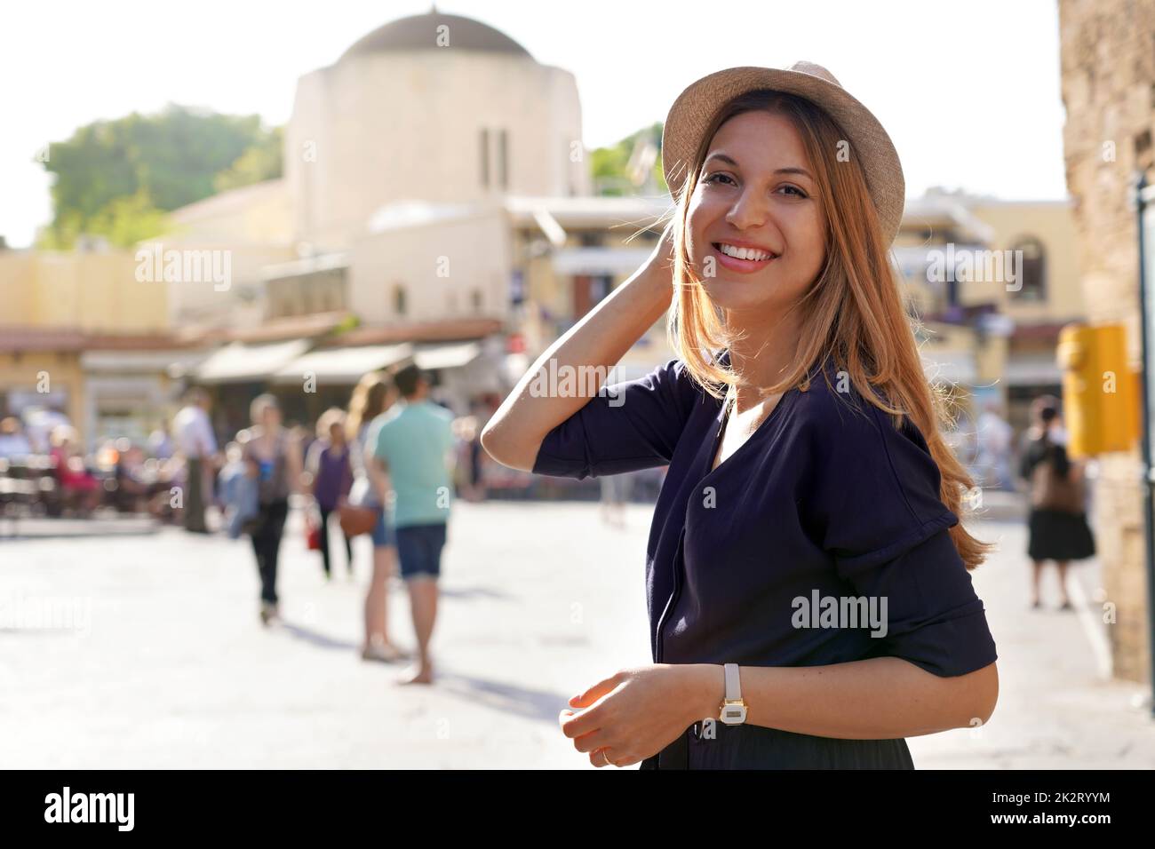 Lächelndes Touristenmädchen, das den Ippokratous Platz in Rhodos Stadt, Griechenland besucht. Schaut auf die Kamera. Stockfoto