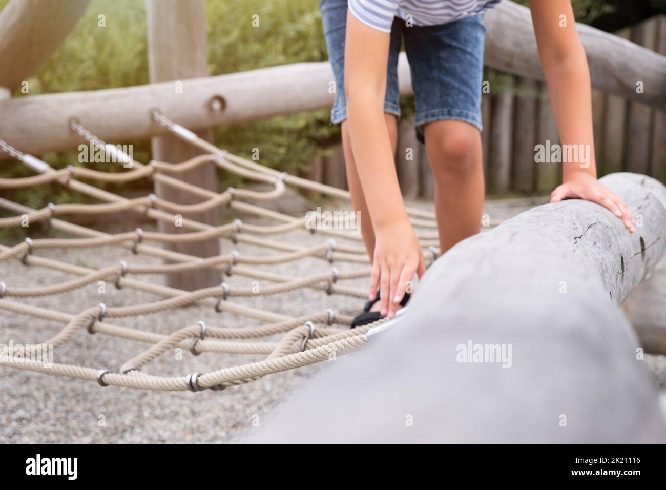 Niedlicher blonder Junge klettert auf einem hölzernen Spielplatz in einem Seilpark. Stockfoto