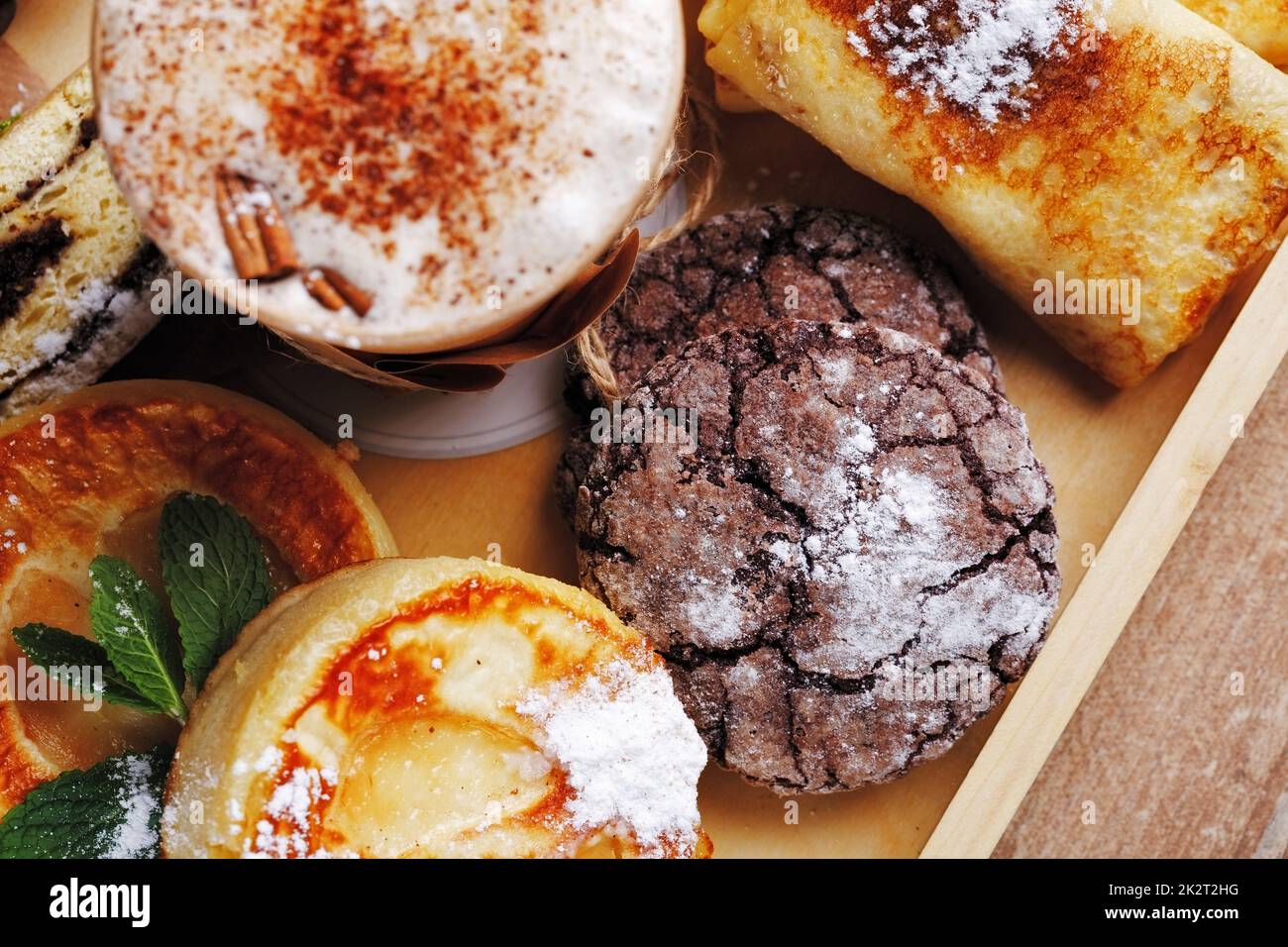 Zimtkaffee und hausgemachte Schokoladenkekse, Strudel- und Minzkäse. Handgemachte Desserts und Kaffee in Papptasse auf braunem rustikalem Holzhintergrund. Stockfoto