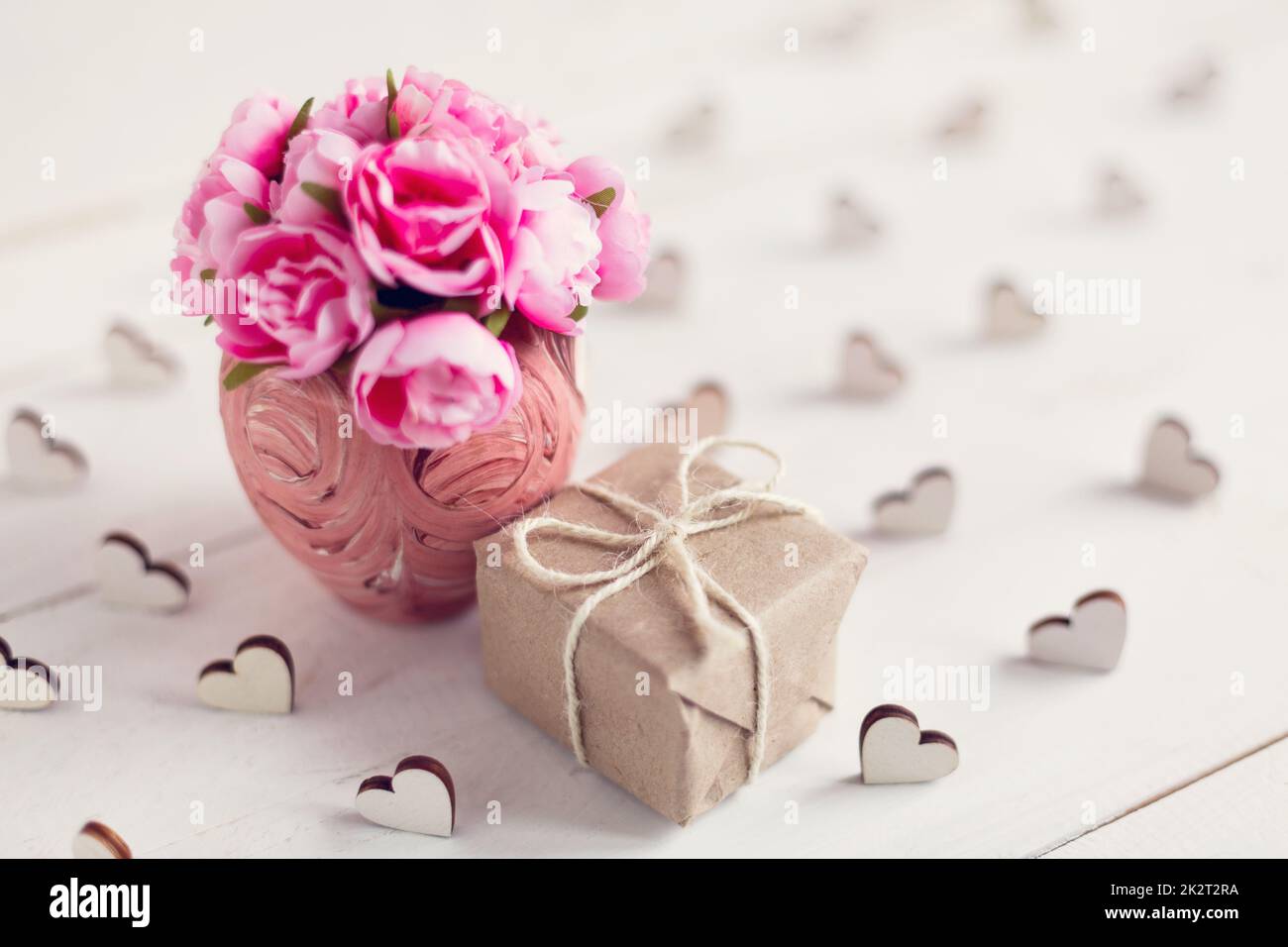 Kleine rosa Rosen in einer schönen Vase und ein kleines Geschenk in Kraftpapier verpackt. Stockfoto