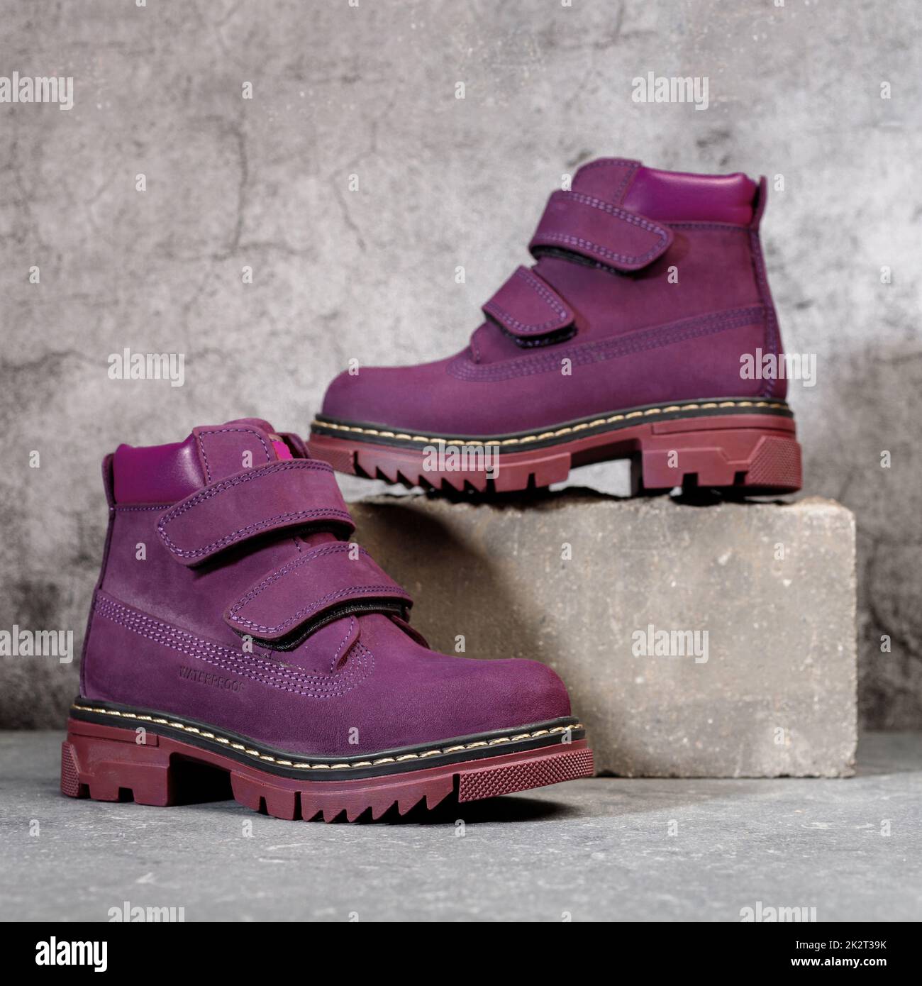 Stylische wasserdichte burgunderrote Damenstiefel mit Klettverschluss auf grauem Beton-Hintergrund. Stockfoto