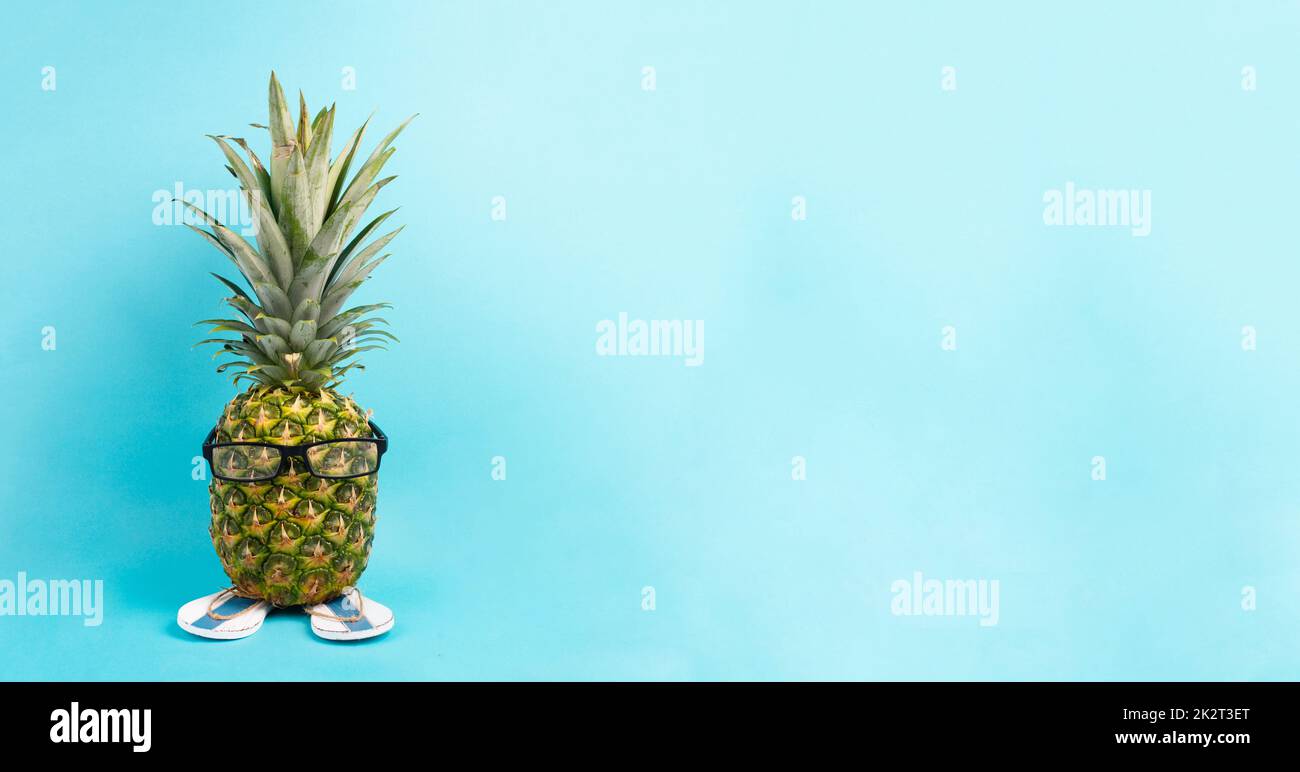 Ananas mit Gläsern und Flip Flops, Urlaubs- und Reisekonzept, tropischer Sommerurlaub, lustige Früchte, blauer Hintergrund Stockfoto