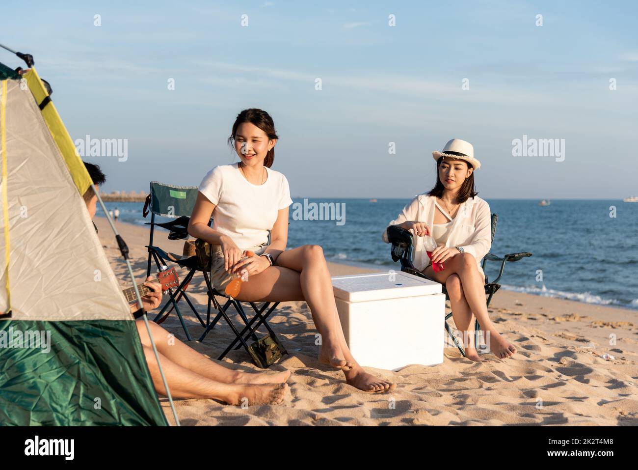 Glückliche Freunde mit Drinks im Camp und gemeinsam lachen im Urlaub am Sandstrand in der Nähe des Campingzelts Urlaubszeit bei Sonnenuntergang Stockfoto