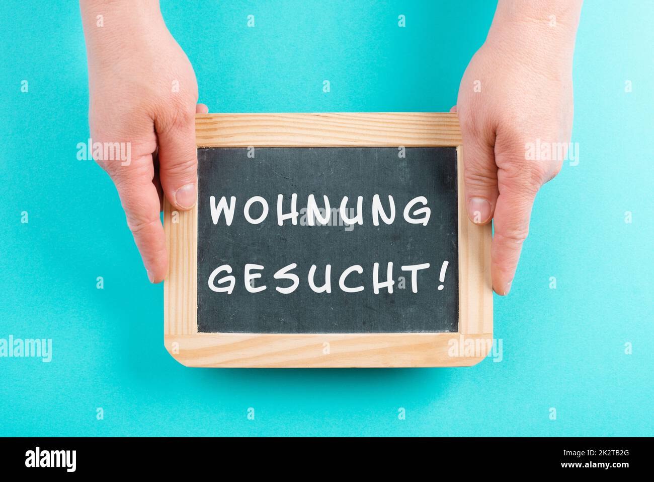 Mit einer Tafel in den Händen steht die Suche nach einer Wohnung in deutscher Sprache auf dem Schild und zieht in ein neues Zuhause, eine Immobilie Stockfoto