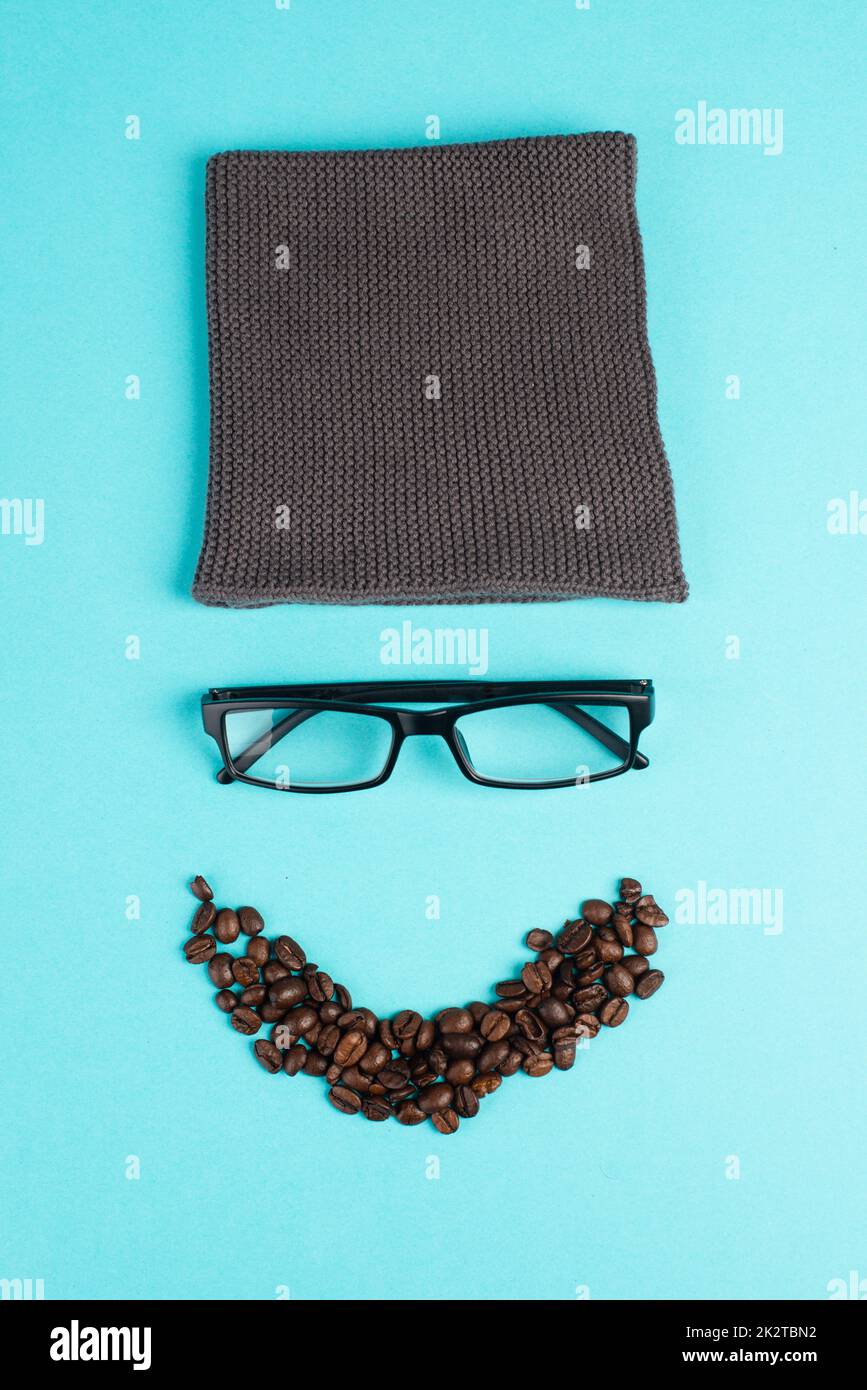 Menschliches Gesicht mit Wollhut, Brille und Kaffeebohnen als Bart, witziges minimalistisches Porträt, Öko-Freak-Lifestyle, Frühstück, Pause Stockfoto