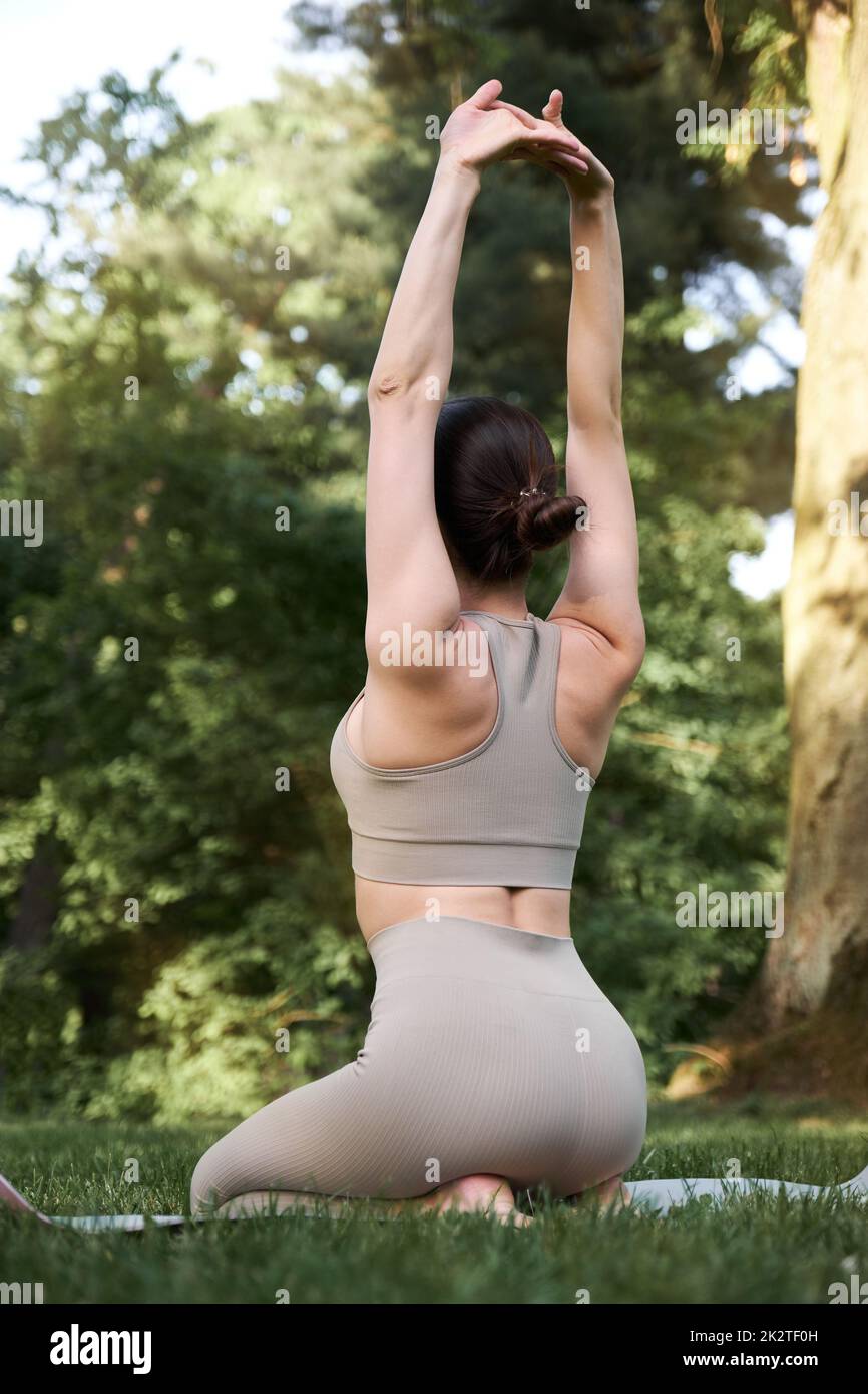 Eine schöne schlanke Frau im Turnanzug übt Yoga und meditiert, während sie auf einer Matte sitzt. Stockfoto