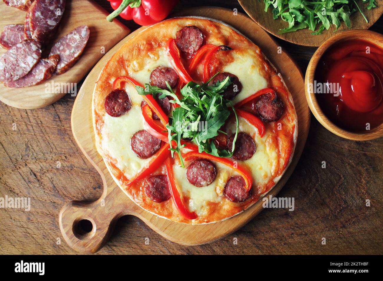 Hot hausgemachte Pizza mit Salami, paprica, Rucola auf hölzernen Tisch. Ansicht von oben Stockfoto