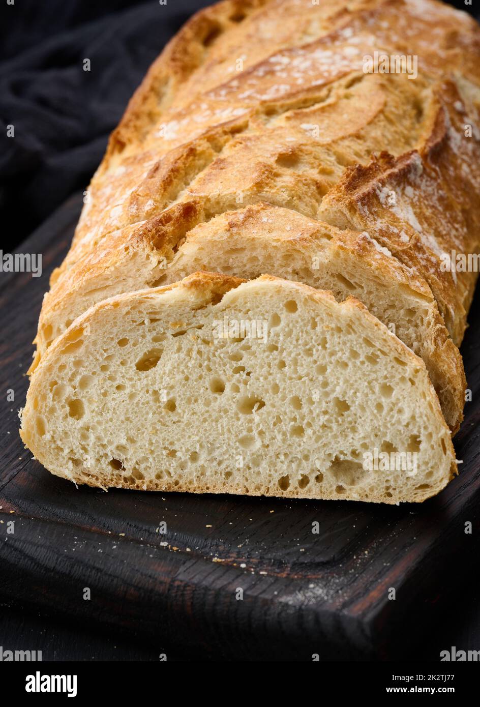 Gebackenes, ovales Vollbrot aus weißem Weizenmehl auf einem schwarzen Tisch, frisches Gebäck Stockfoto