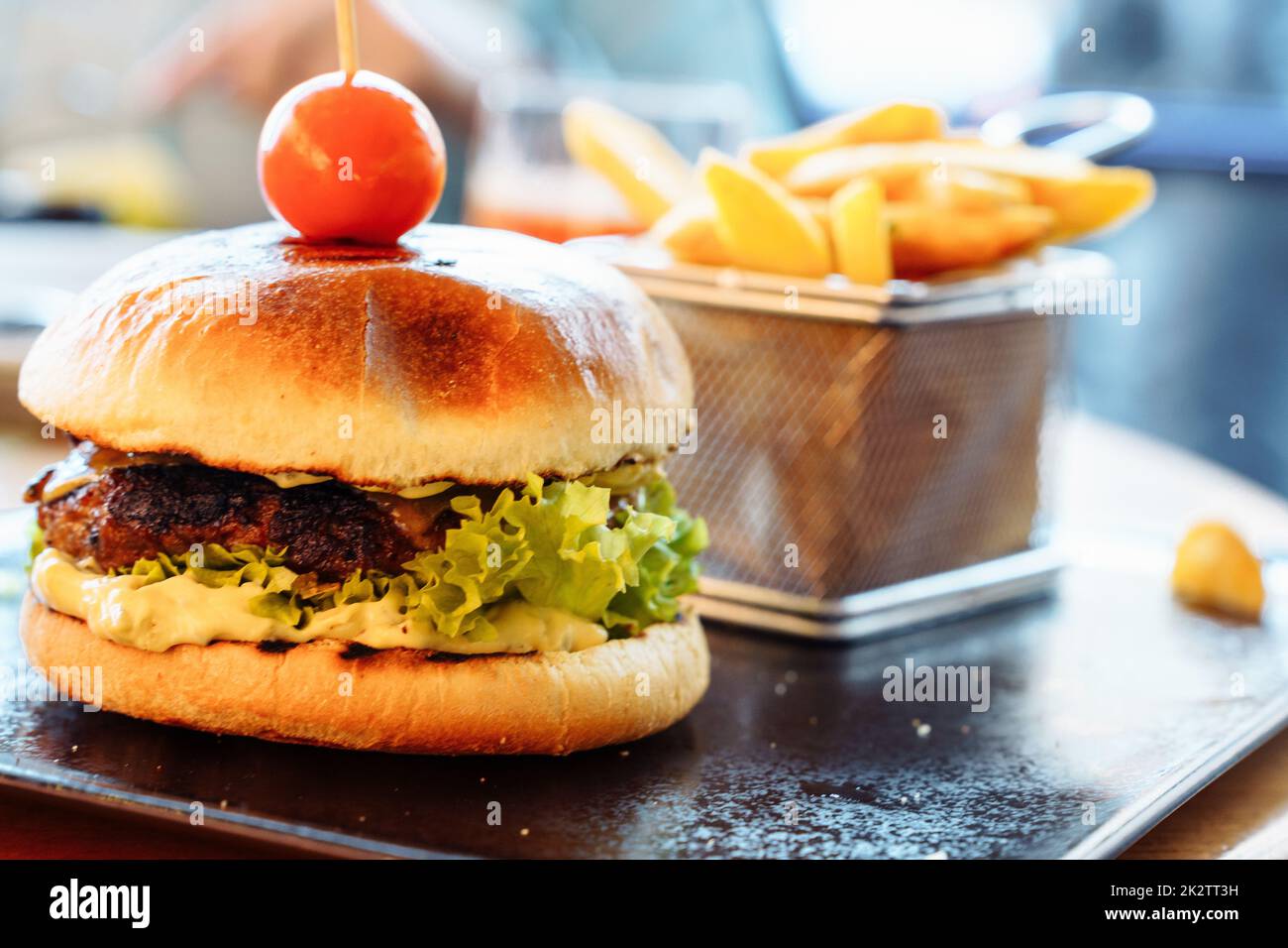 Ein selektiver Fokus auf einem frischen Burger mit Pastete, Kirschtomaten und Salat. Pommes frites im Hintergrund Stockfoto