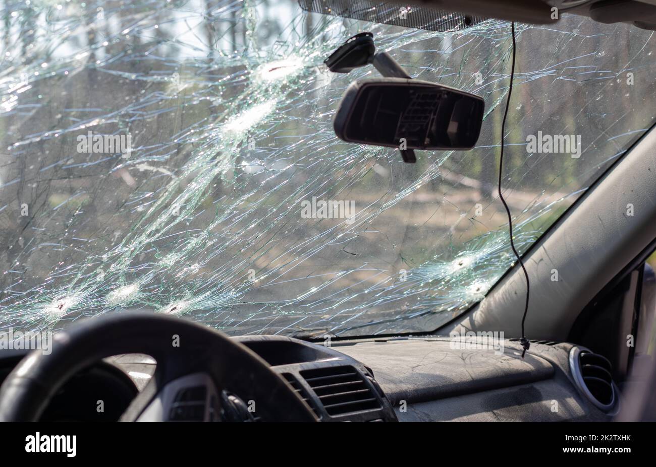 Gebrochene Windschutzscheibe eines Autos durch eine Kugel, durch einen Schuss von einer Waffe, Blick von der Innenseite der Kabine. Beschädigtes Glas mit Spuren eines entgegenkommenden Steins auf der Straße. Innenansicht des Fahrzeugs. Stockfoto