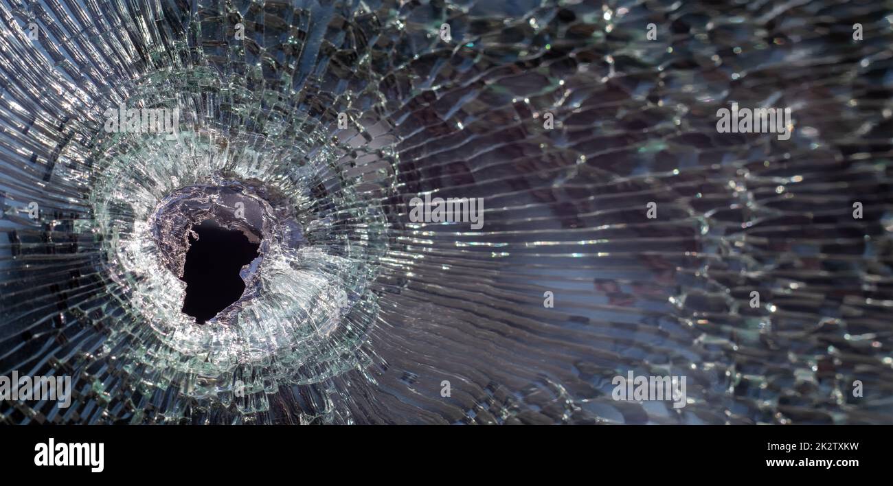 Einschussloch in Glas mit Rissen, echte Einschussloch-Nahaufnahme. Die Kugel hat ein Rissloch in der Windschutzscheibe eines Autos oder ein zerbrochenes Fensterglas infolge eines Unfalls verursacht. Banner mit Kopierbereich. Stockfoto