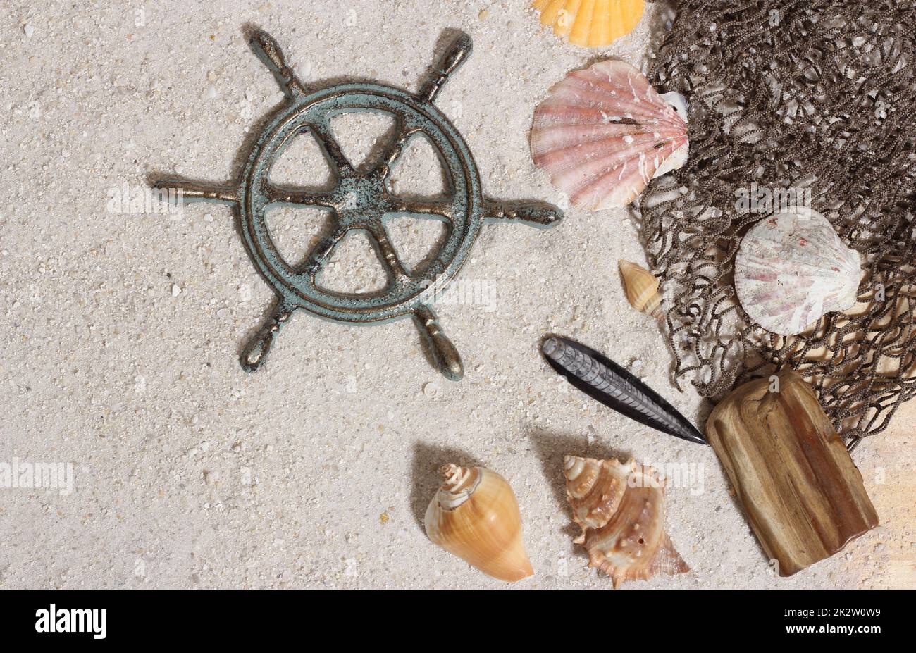 Kapitänsrad mit Fischernetz und Meeresmuscheln im maritimen Sand-Hintergrund Stockfoto