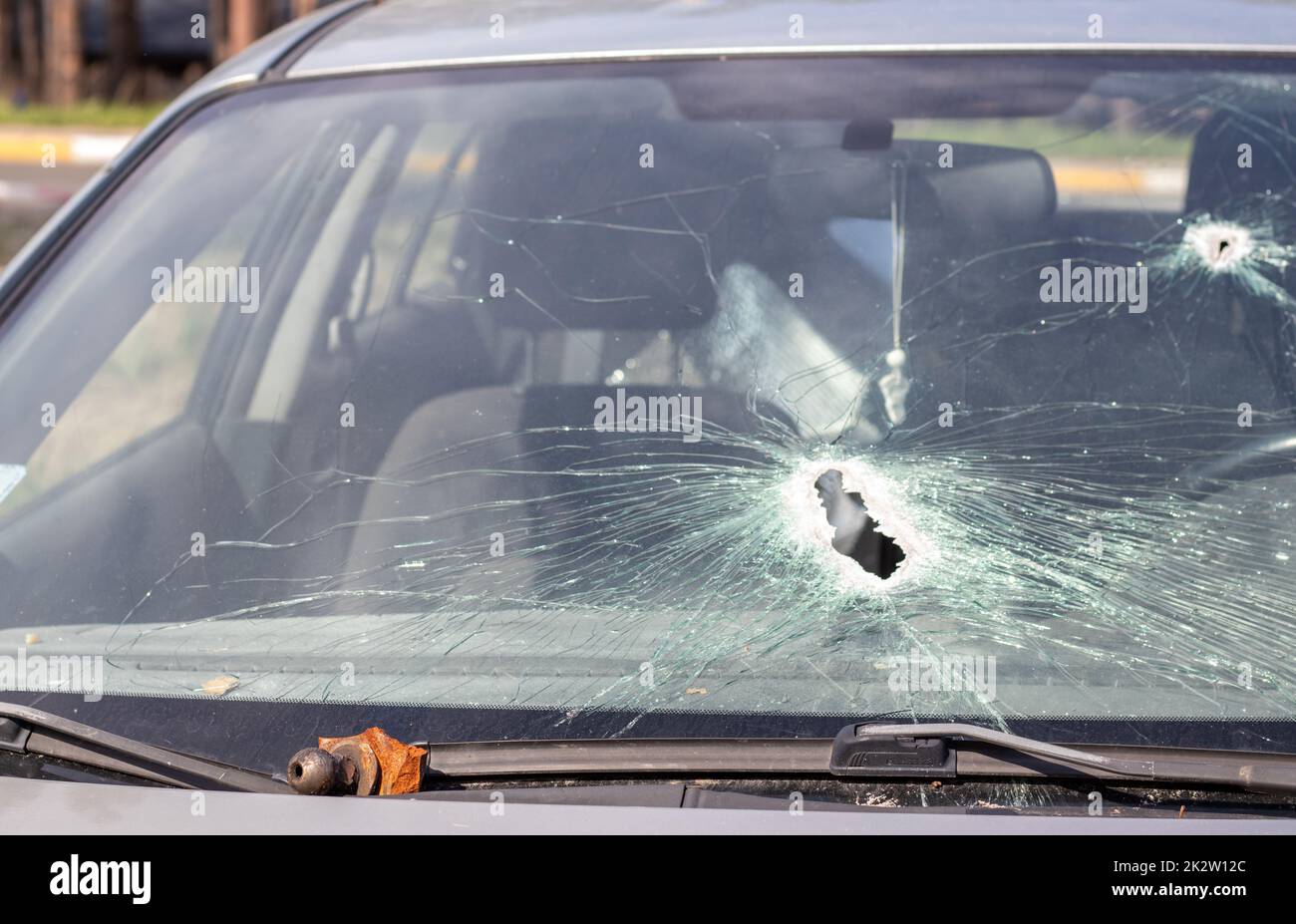 Löcher auf der Windschutzscheibe des Autos, es wurde von einer Waffe erschossen. Einschusslöcher. Zertrümmere die Windschutzscheibe, zerbrochenes und beschädigtes Auto. Die Kugel hat ein Loch im Glas zerbrochen. Stockfoto