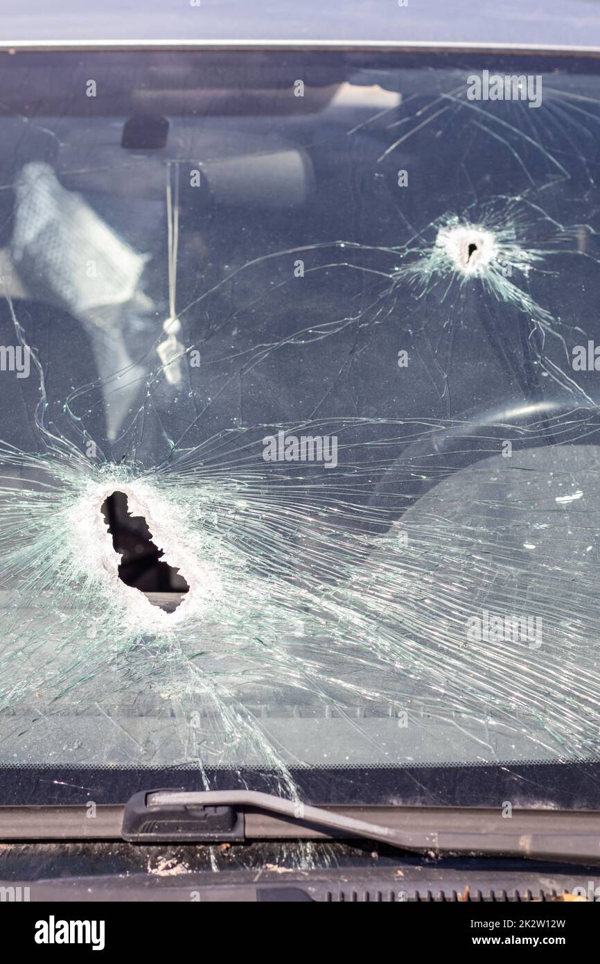 Löcher auf der Windschutzscheibe des Autos, es wurde von einer Waffe erschossen. Einschusslöcher. Zertrümmere die Windschutzscheibe, zerbrochenes und beschädigtes Auto. Die Kugel hat ein Loch im Glas zerbrochen. Stockfoto
