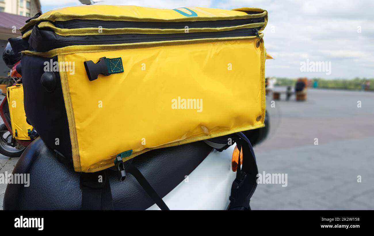 Kuriermotorroller mit gelbem Rucksack. Ein Fahrer auf einem Roller wartet auf eine Bestellung. Schnelle Lieferung von Waren an Kunden vom Restaurant und Geschäft. Kopieren Sie Platz auf der Tasche. Stockfoto