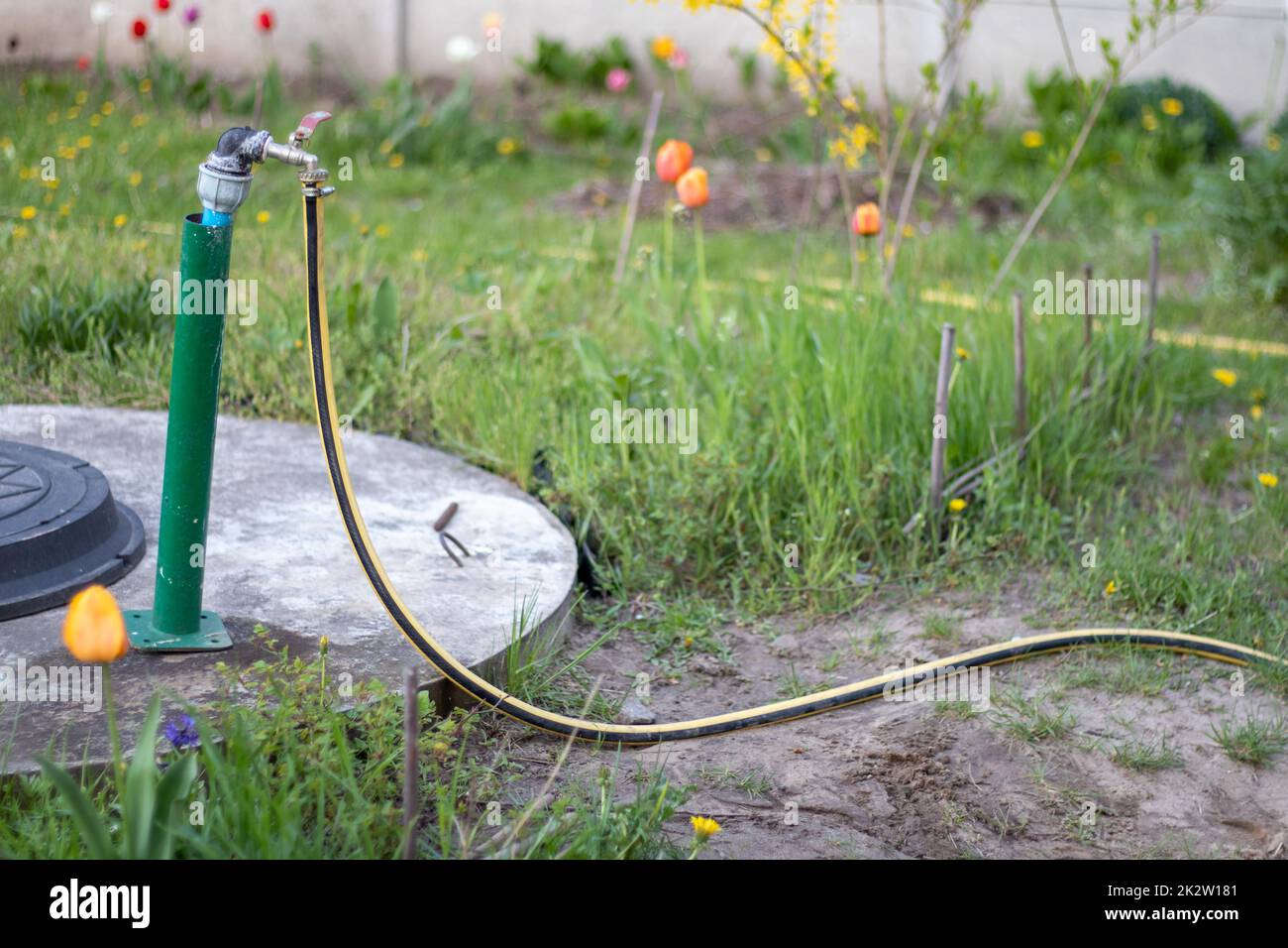 Rohrleitungen, Wasserpumpe aus einem Brunnen. Ein Außenwasserhahn mit einem gelben Gartenschlauch. Bewässerungswasserpumpensystem für die Landwirtschaft. Schlauch im Garten zum Bewässern, sonniger Sommertag. Stockfoto