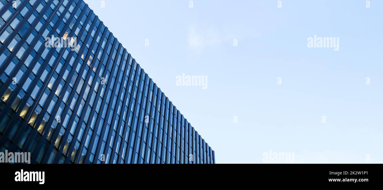 Modernes Hochhaus am blauen Himmel. Blick von unten auf einen Wolkenkratzer im Geschäftsviertel. Blick auf die Glasfassade eines Bürogebäudes aus einem niedrigen Winkel. Banner mit Kopierbereich. Stockfoto