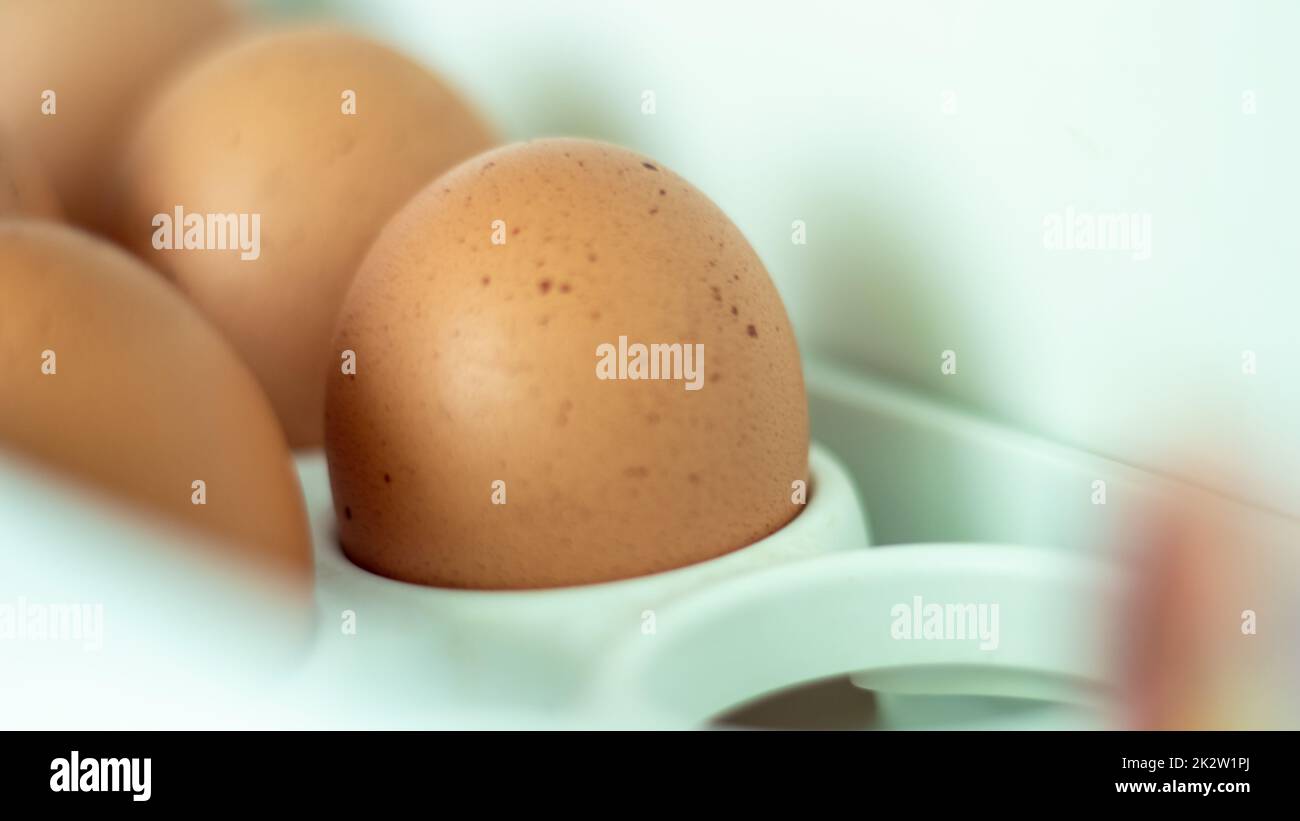 Rohe Hühnereier im Kühlschrank, Nahaufnahme. Braune Eier in einem Eiertuch auf einem Regal an der Kühlschranktür. Ausgewählter Fokus. Stockfoto