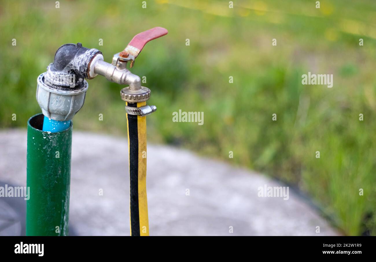 Rohrleitungen, Wasserpumpe aus einem Brunnen. Ein Außenwasserhahn mit einem gelben Gartenschlauch. Bewässerungswasserpumpensystem für die Landwirtschaft. Schlauch im Garten zum Bewässern, sonniger Sommertag. Stockfoto